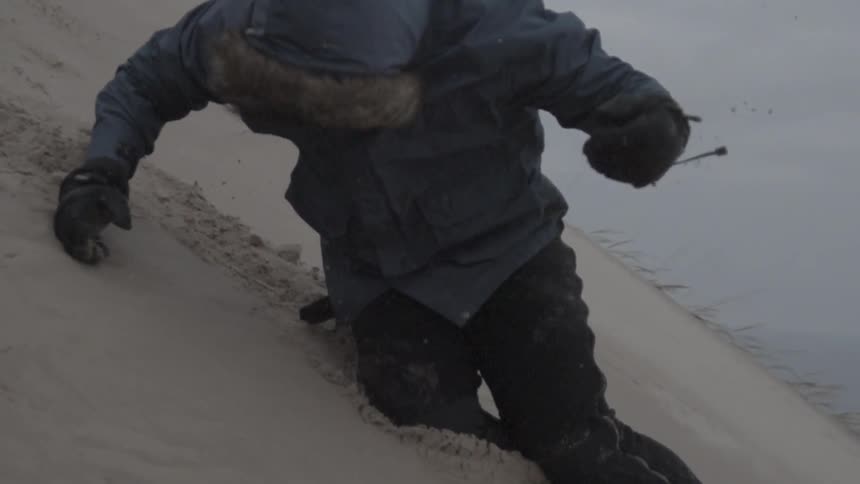 A man dressed in winter clothing falls down the side of a hill in the desert