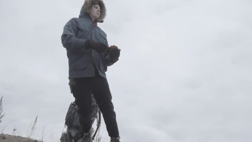 A man in a parka with a backpack and holding a gun falls to the ground