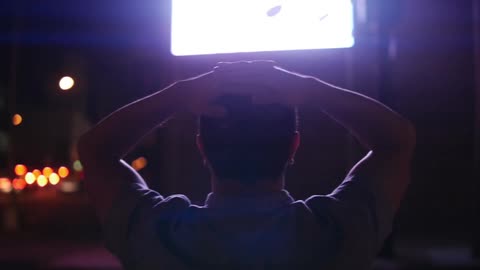 A man watches a screen with his hands on his head