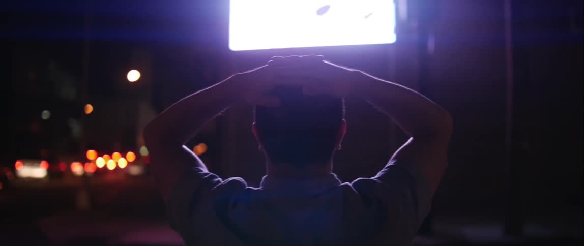 A man watches a screen with his hands on his head