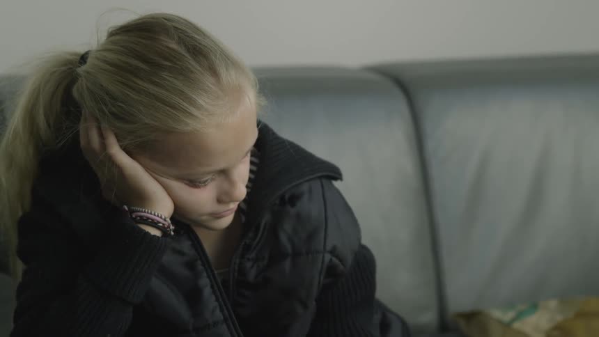A girl sits as a hand touches her on the shoulder