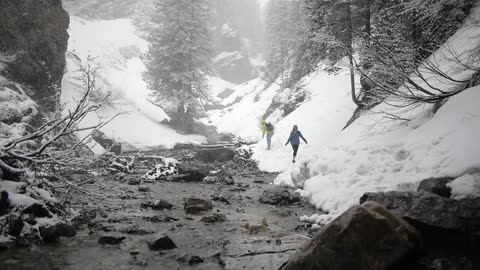Two people walk along a snow covered river bank as snow falls
