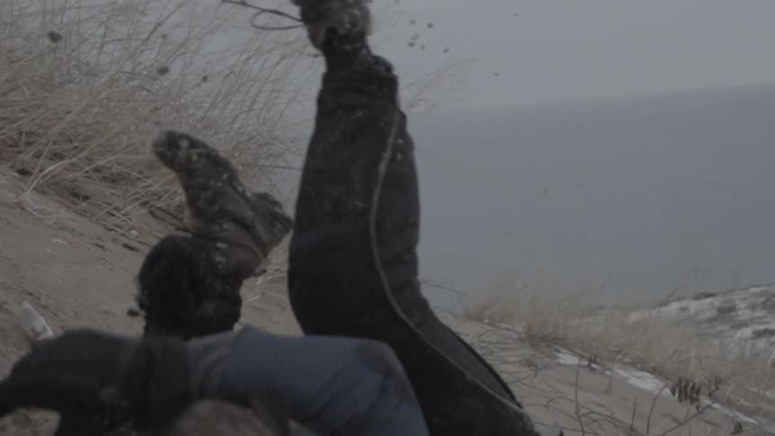 A person wearing a heavy coat and gloves rolls down a rural hillside