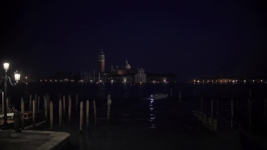 A boat cruising away from docks at night while lights shine from buildings in the background