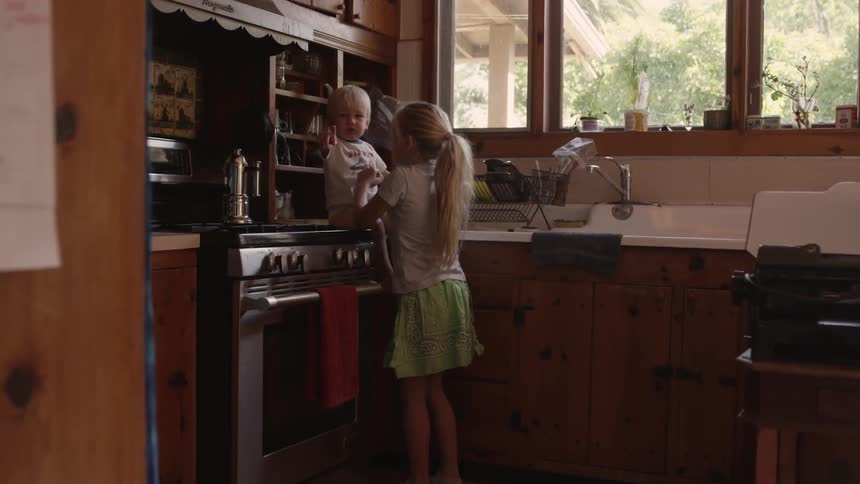 Little girl puts a little boy on a cabinet in kitchen