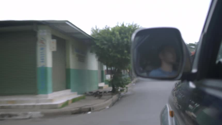 A view of a man in a side mirror as he drives down a narrow urban street