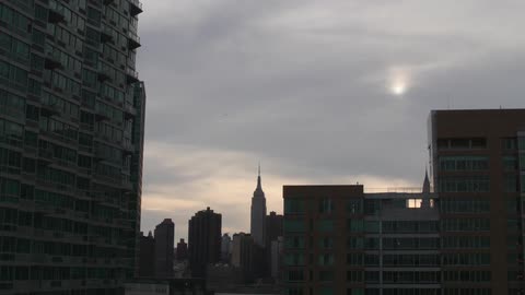 A timelapse view of clouds and the sun moving across the sky over tall city buildings