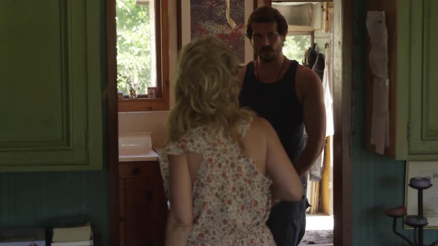 A woman walking towards a doorway and stopping as a man holding a beer bottle says something to her before walking away