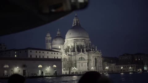 Buildings are viewed by a group across water at night