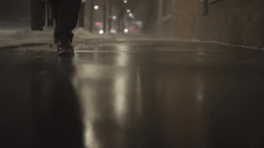 Feet shuffle through snow on a city street at night