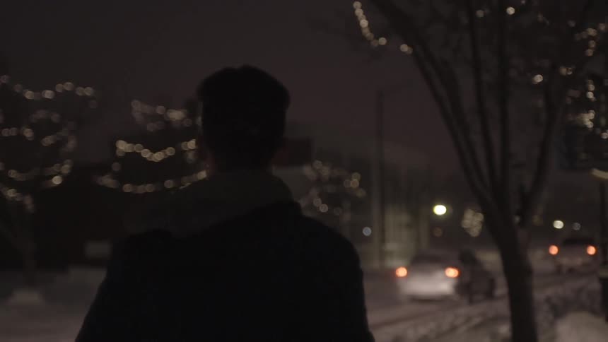 A man walks down a snowy city sidewalk at night