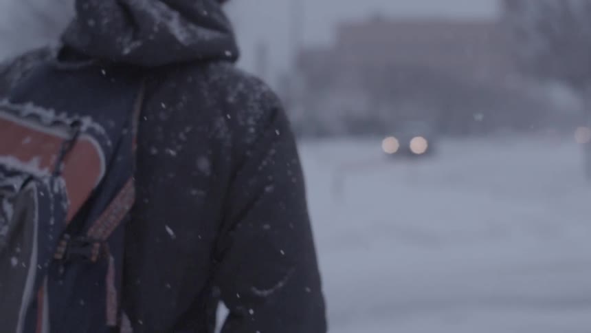A young man walking in the snow in an urban area as a car approaches