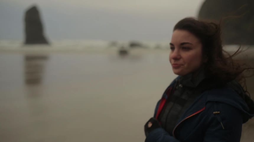 A woman stands on a windy beach and smiles