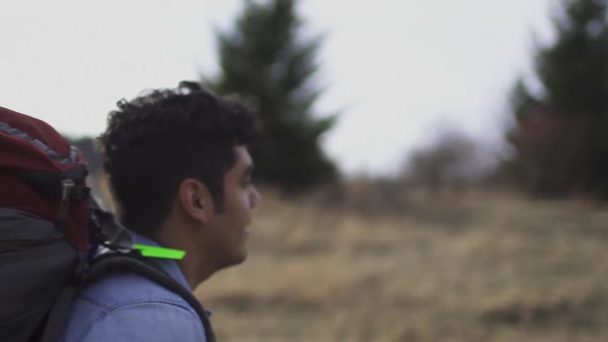 A young man wearing a large backpack and looking across the horizon as he smiles