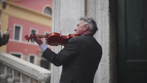 A man plays a violin in front of a building