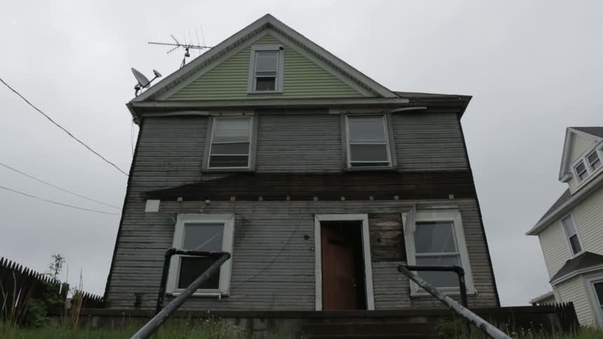 A derelict house stands in a neighborhood