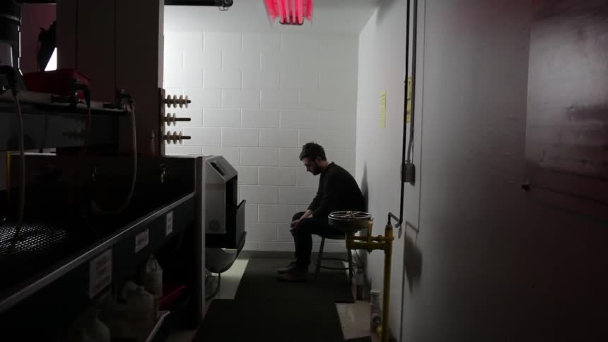 A man walks into a lab and sits on stool to wait for something to print