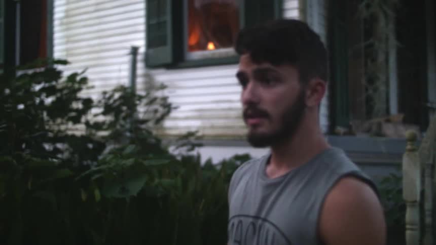Man walks in front of a home smoking a cigarette