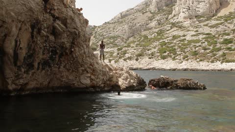 Young man jumping from a tall rock into the water