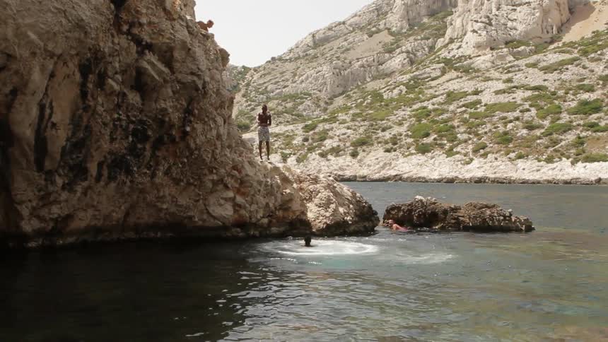 Young man jumping from a tall rock into the water