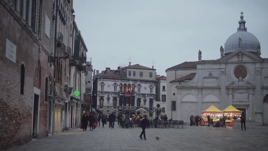 Two boys kicking a football in a city square with people and buildings in the background