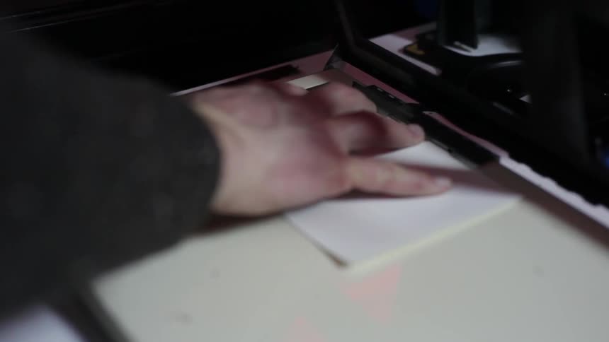 A persons hand putting a piece of paper in a printer