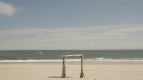 A shade structure on the beach as waves crash to shore