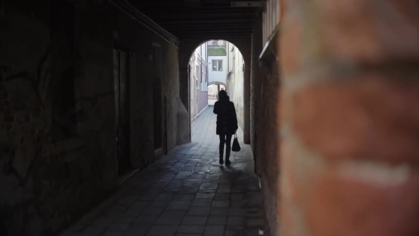 A person holding a bag walks down a dark alley