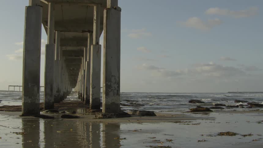 Wet sand under pier supports as waves crash on shore