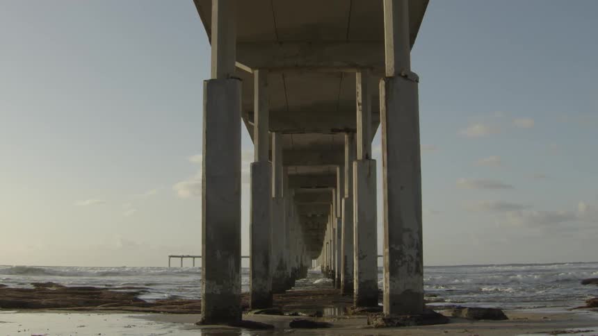 Wet sand under a pier as waves roll on shore in the background