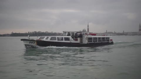 A boat travelling over water with buildings and heavy clouds in the background