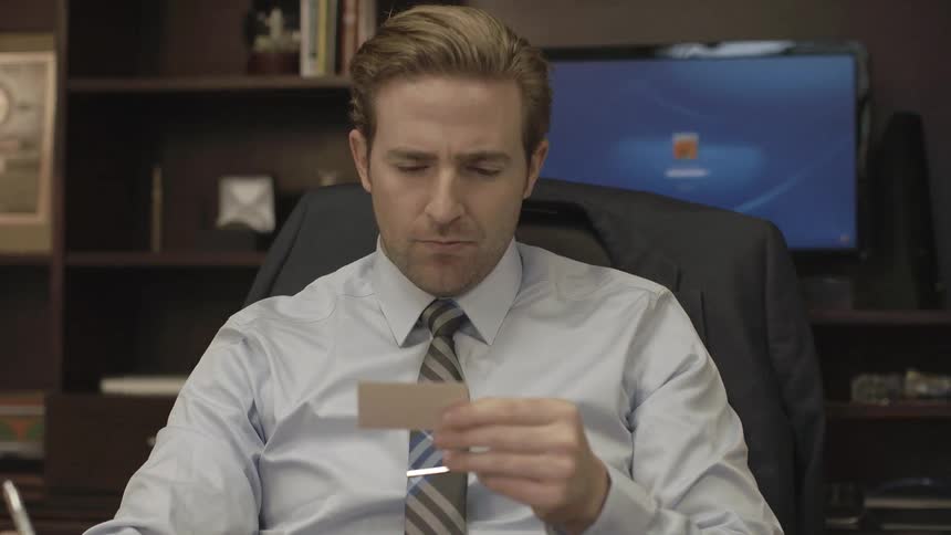 A man sits at a desk and reads a card