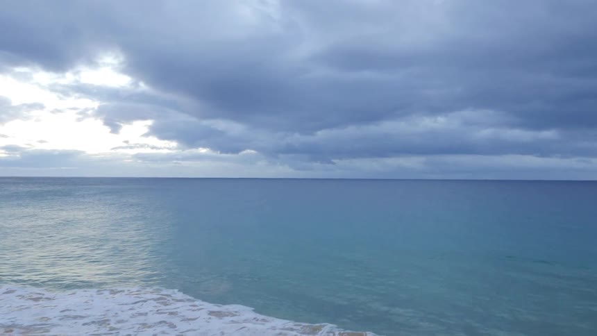 View of a ocean moving to a shore on a cloudy day