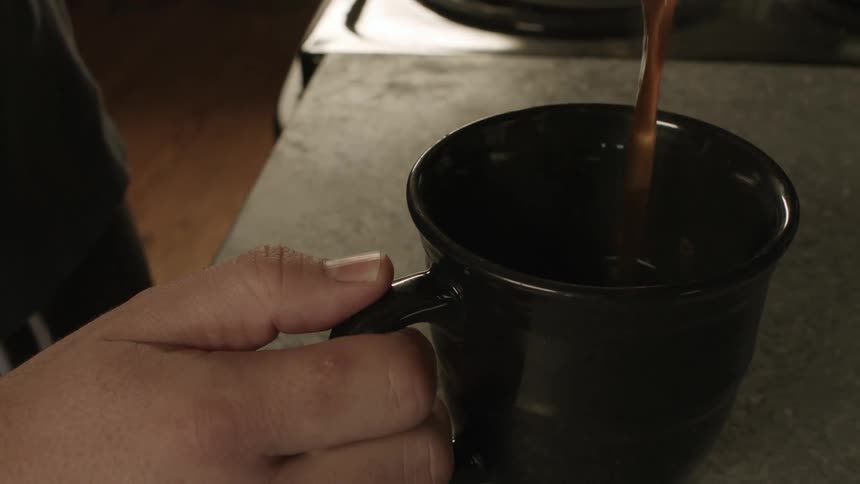 Man pouring brown steaming liquid into a mug