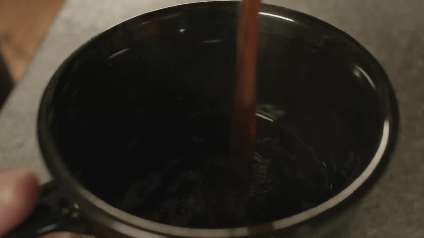 Steaming brown liquid being poured into a mug