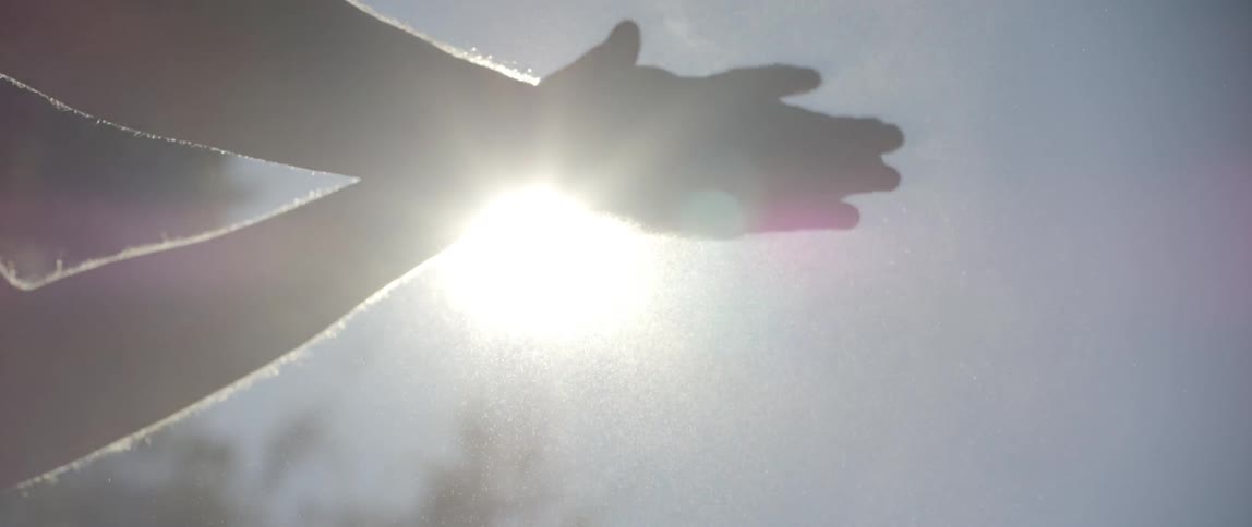 An outstretched hand with the sun glaring behind it before the person stretches out the other arm and wipes something off their hands