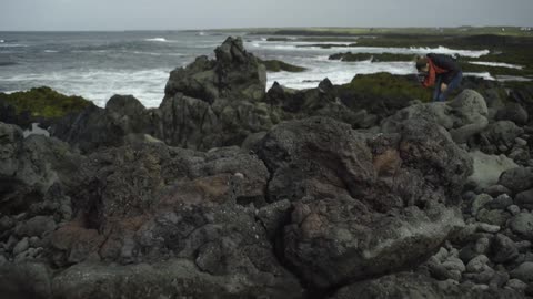 A woman photographs boulders on the beach