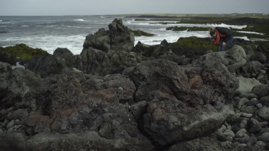 A woman photographs boulders on the beach