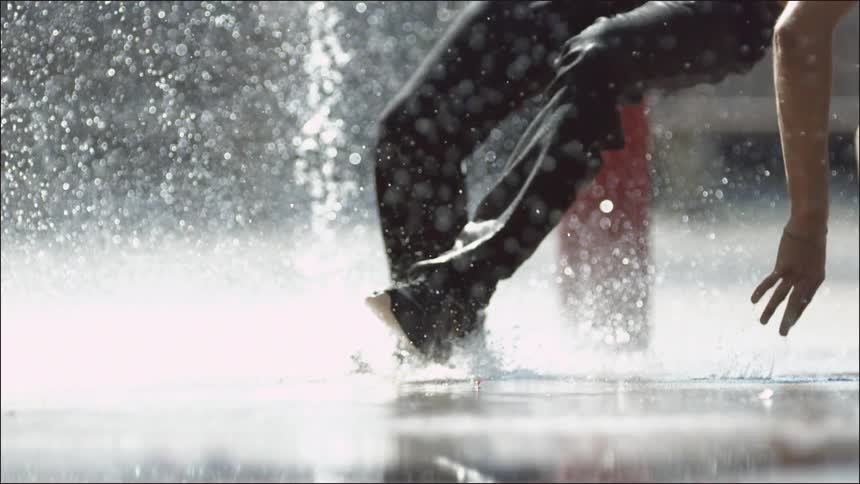 Person breakdancing on some wet pavement while being showered with water