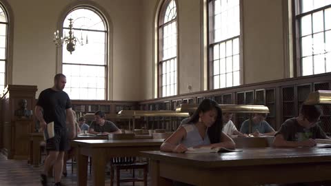 Man walking to a desk with a book and sitting down in a library
