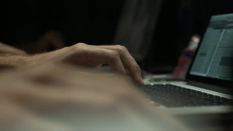 The hands of two people working on laptops