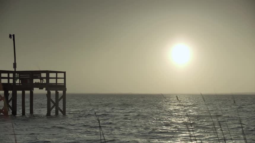Sun going down over the water, beside a pier