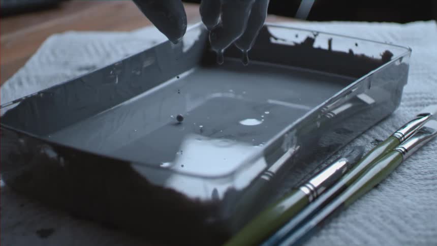 Hand dripping paint from his covered hand into a paint pan