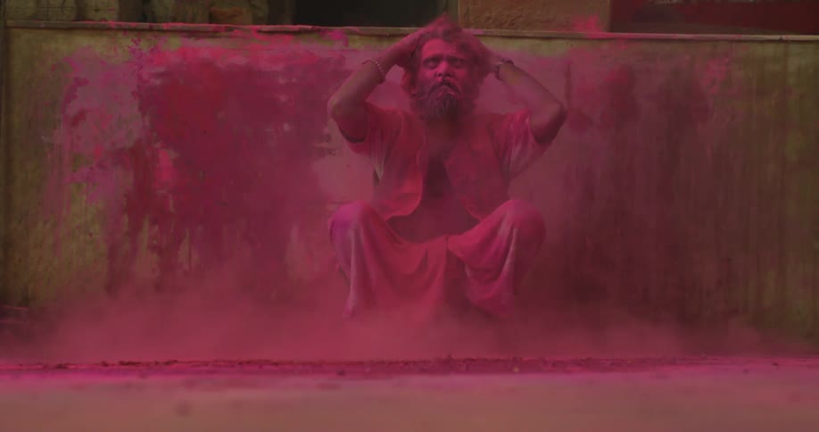A man stooping down covered in pink powder