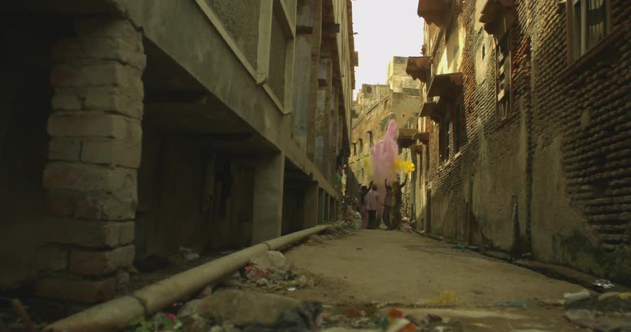 A group stand in a narrow alley between homes and throw up colored powder in celebration