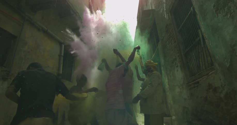 Men standing in a gangway as they throw red, yellow and green powder into the air