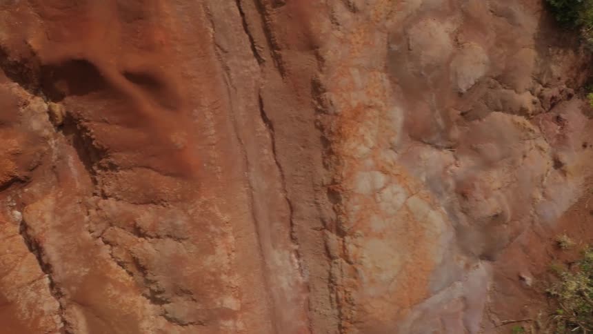 A rocky, red cliff side with brush growing on it