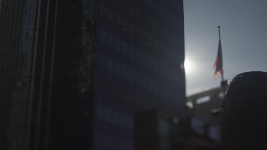A woman walks in the city as an american flag billows in the background