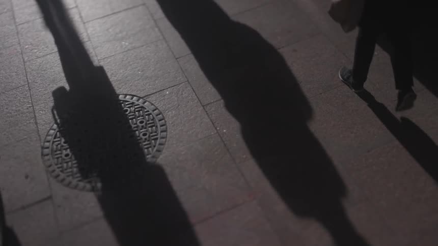 The people walk by giving shadows off on the sidewalk