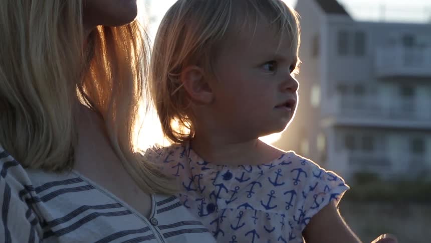 Blonde woman with sunglasses holding a blond toddler at sunset